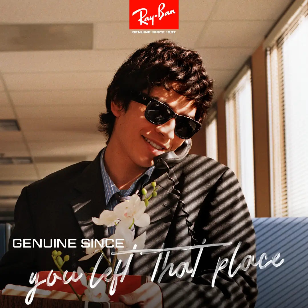 Smiling man wearing Ray-Ban sunglasses, talking on a landline phone, holding flowers, with the text 'Genuine Since You Left That Place' and the Ray-Ban logo above.